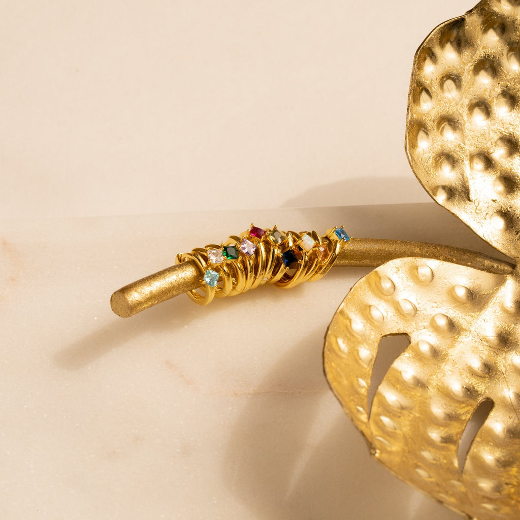 Athena Opal Huggies with vibrant gemstones stacked on a golden branch beside a decorative gold leaf.