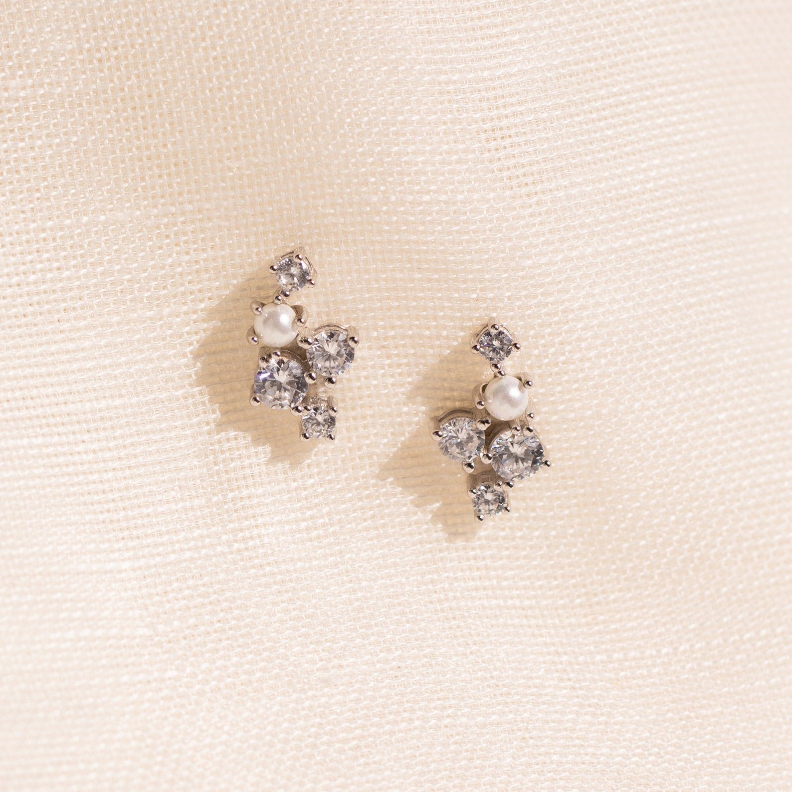 A pair of Seine Diamond Studs featuring cultured pearls and sparkling gemstones, displayed on a soft cream fabric background—perfect as elegant wedding earrings.