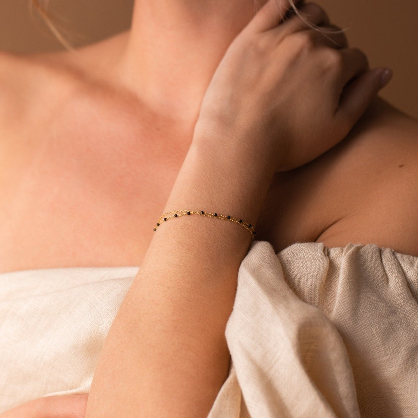 Woman in an off-shoulder beige top wears a delicate gold bracelet with black accents, ideal for stacking or pairing with a boho style like the Calypso Station Bracelet.