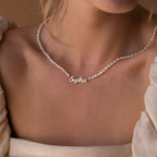 A woman wears the Mellow Pearl Name Necklace—a delicate nameplate reading "Sophia" with elegant pearls—styled with a cream off-shoulder top.