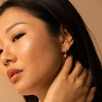 Close-up of a woman touching her ear, wearing the Pave Initial Huggies—small, elegant gold earrings shaped like the letter K—perfect as a personalized gift.