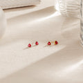 Ruby Heart Studs—gold earrings featuring small ruby heart-shaped studs displayed on a beige textured surface with soft lighting, perfect for adding a romantic touch to your date night look.