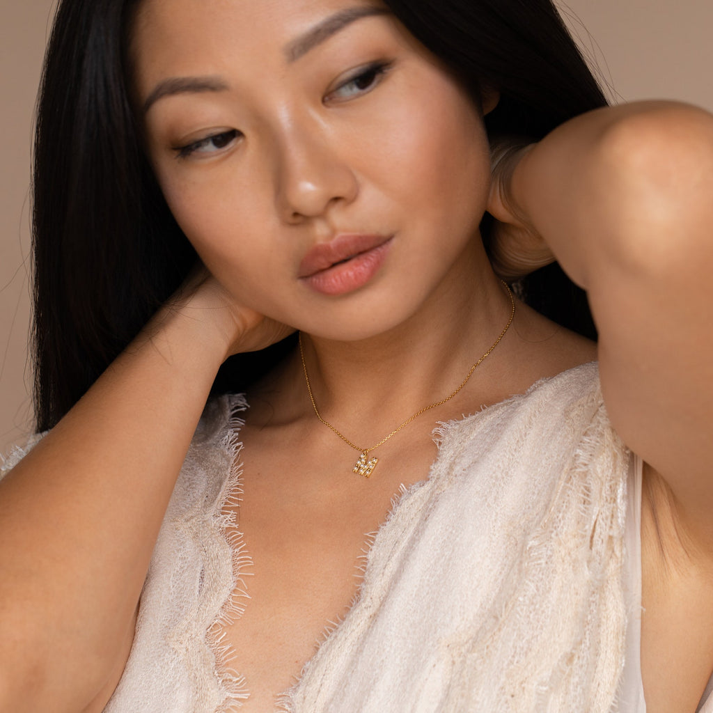 Woman in a textured cream top adjusts her hair while wearing the Pearl Letter Necklace, a gold personalized jewelry piece with a small pendant.