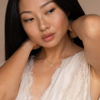 Woman in a textured cream top adjusts her hair while wearing the Pearl Letter Necklace, a gold personalized jewelry piece with a small pendant.