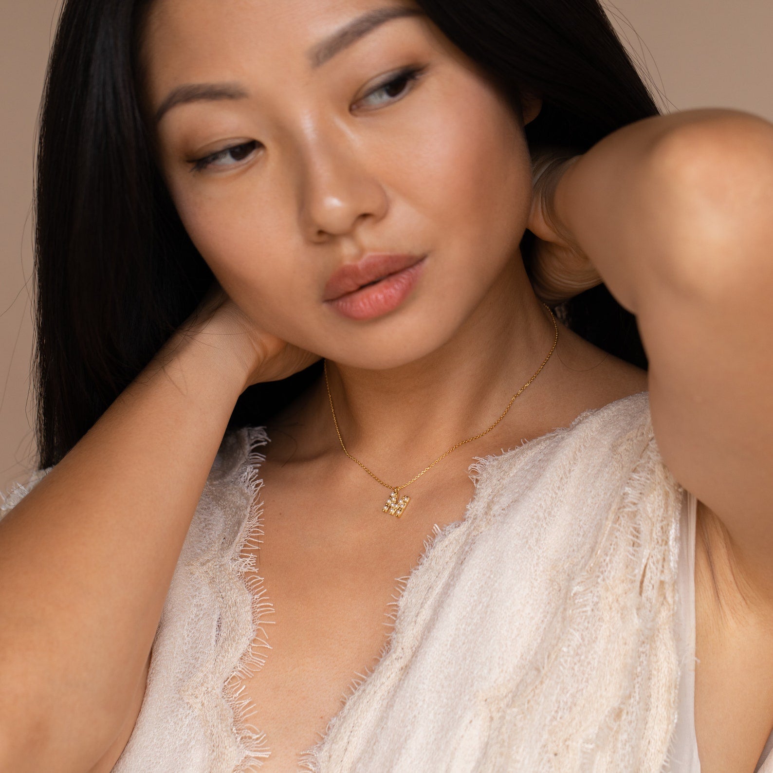 Woman in a textured cream top adjusts her hair while wearing the Pearl Letter Necklace, a gold personalized jewelry piece with a small pendant.