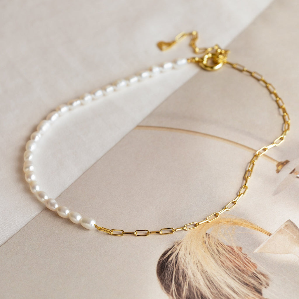 Two-tone necklace with half white freshwater pearls and half elongated gold chain links, displayed on a neutral background with a magazine page.

