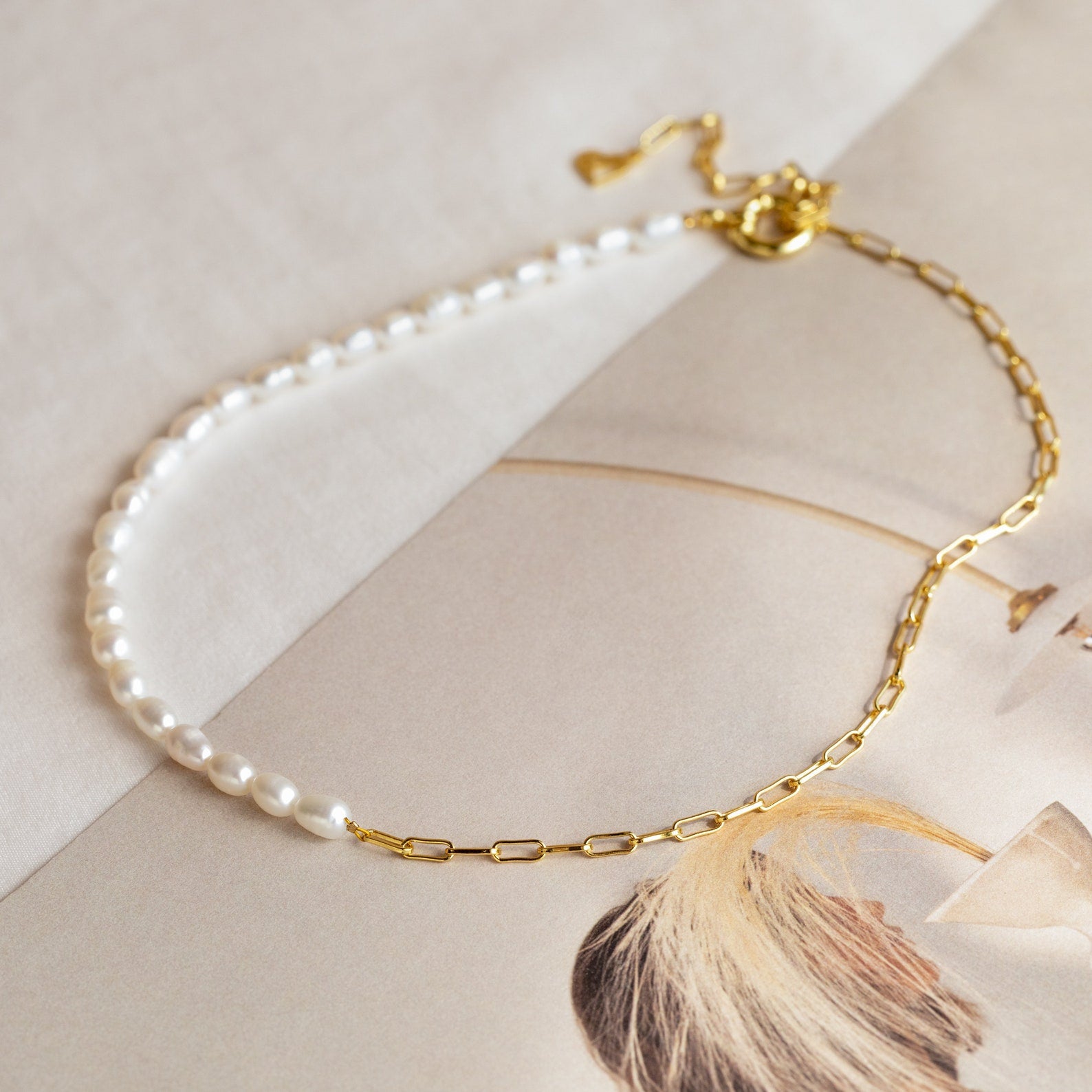 Two-tone necklace with half white freshwater pearls and half elongated gold chain links, displayed on a neutral background with a magazine page.

