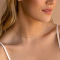 Woman wearing a delicate silver chain choker with small faceted links, styled with a white spaghetti strap top.