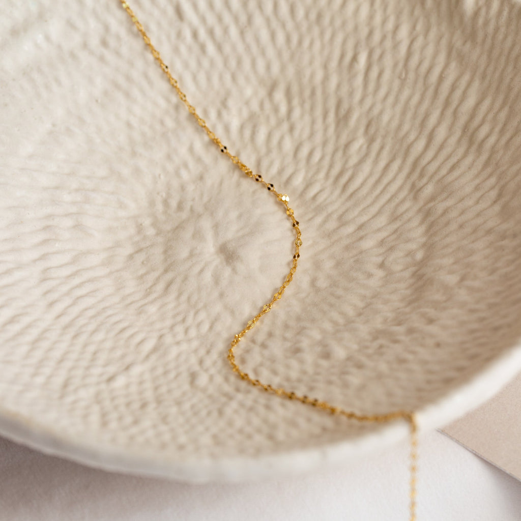 A delicate gold Josephine Chain Necklace lies inside a textured, off-white ceramic bowl—an elegant accent for wedding jewelry displays.