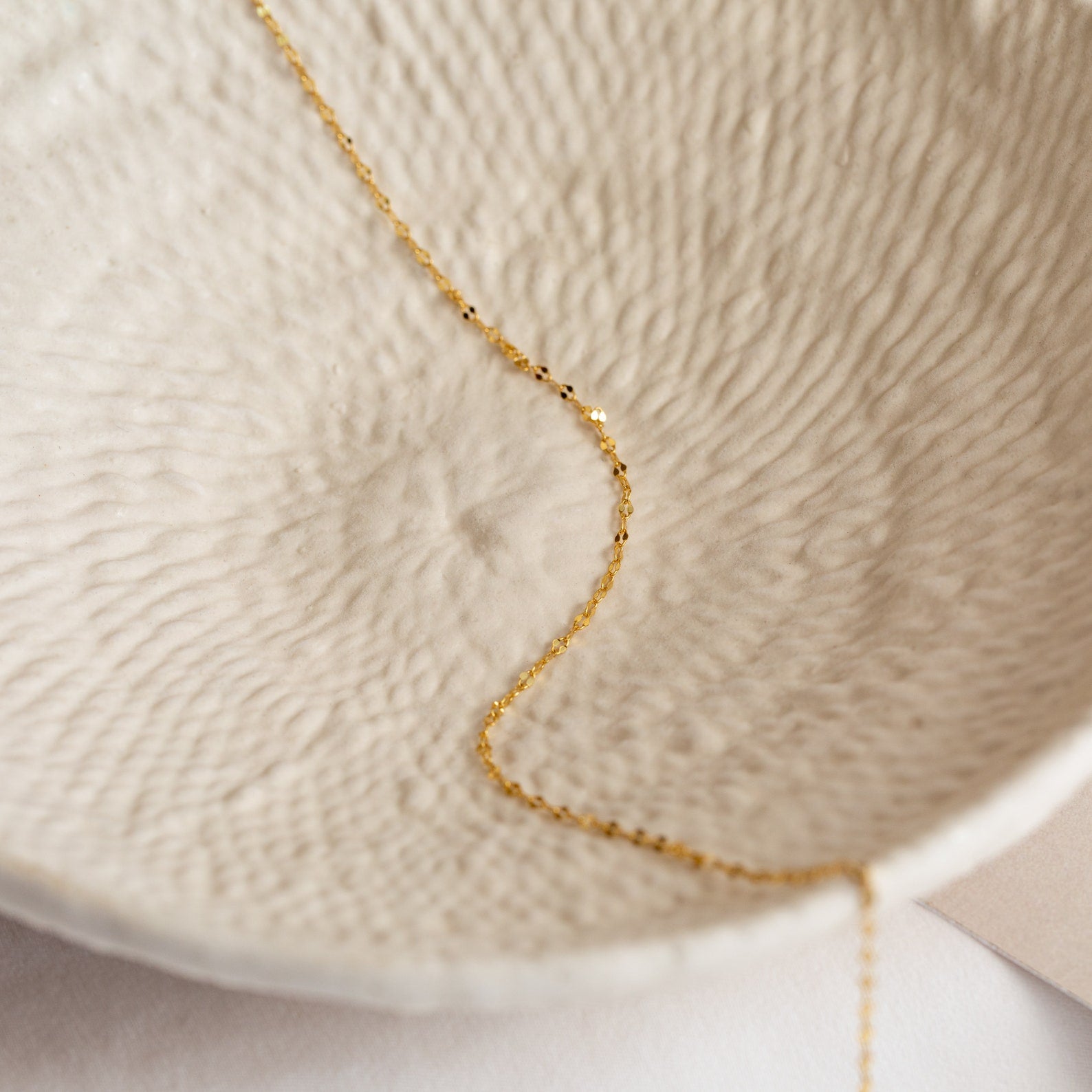A delicate gold Josephine Chain Necklace lies inside a textured, off-white ceramic bowl—an elegant accent for wedding jewelry displays.