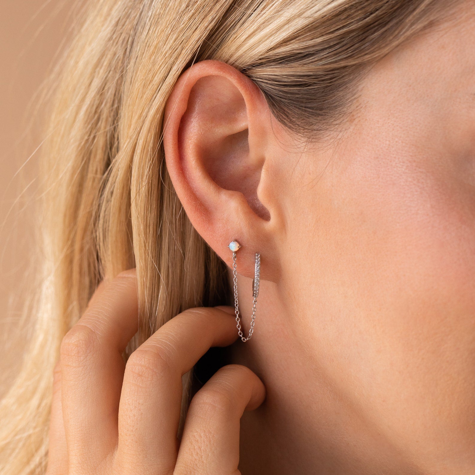 Close-up of a woman's ear wearing Opal Stud & Pave Hoop Earrings—a versatile silver chain earring with a small opal stud—while her hand rests near her ear.