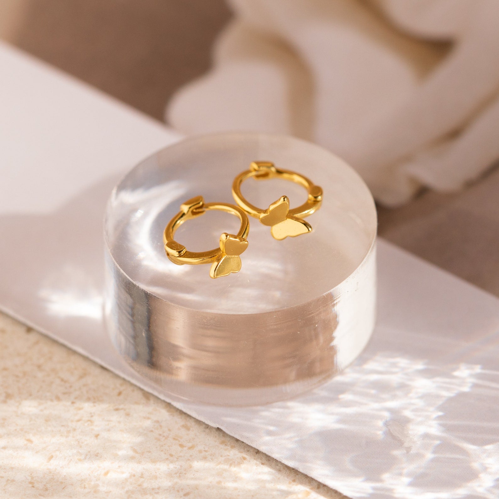 Flat lay of cartilage huggies over a small transparent surface with bright lighting to highlight gold tone.