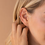 Close-up of a hand near styled mini sterling silver huggie hoop, adorned with a tiny butterfly charm in front, showing delicate polished fit.