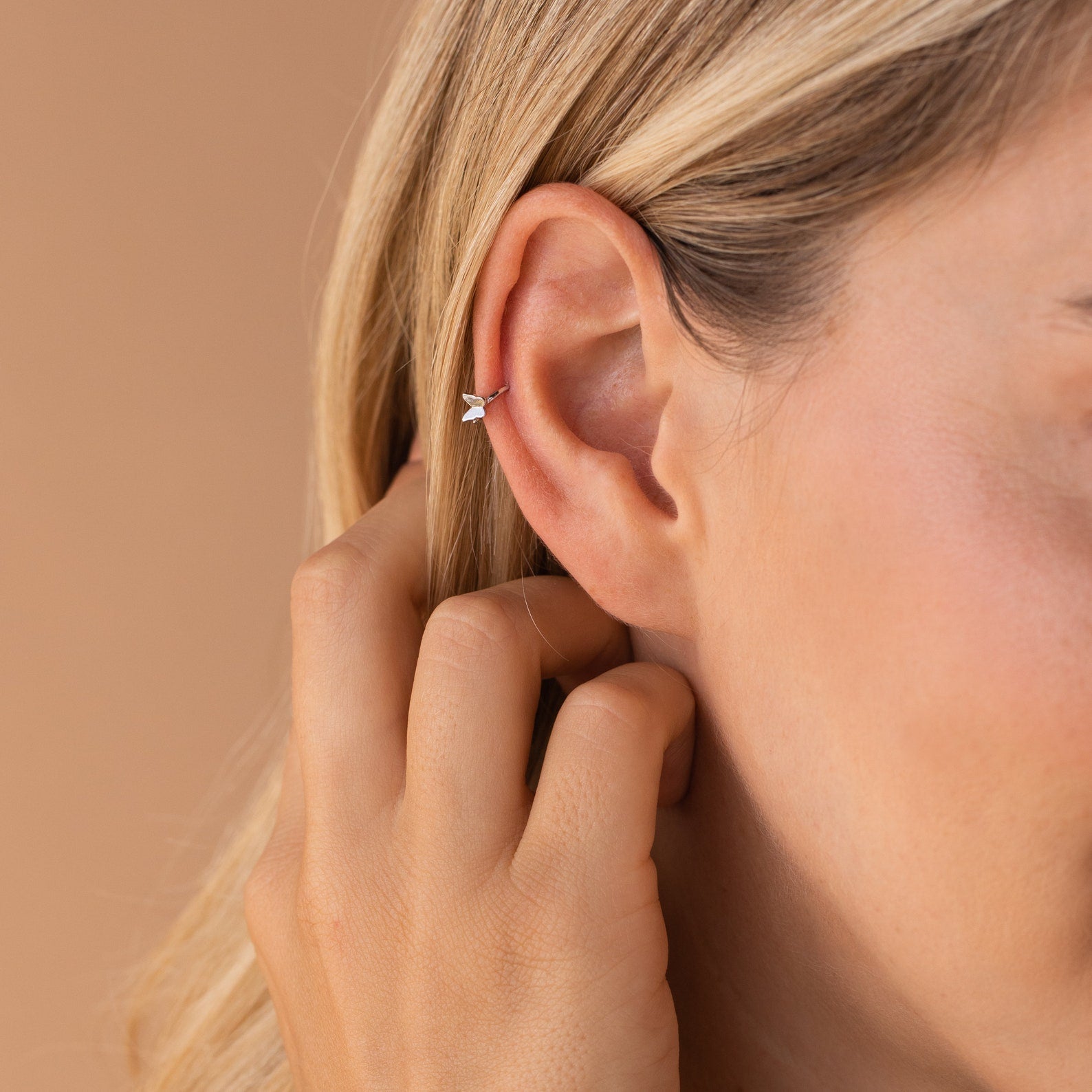Close-up of a hand near styled mini sterling silver huggie hoop, adorned with a tiny butterfly charm in front, showing delicate polished fit.