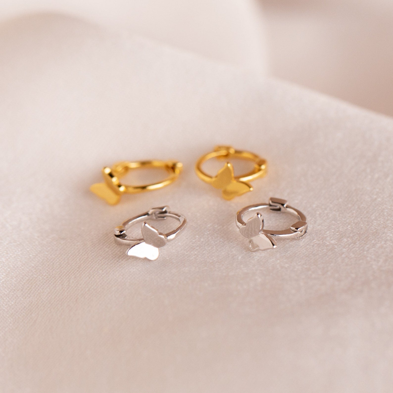 Flat lay of two pairs of earrings (gold and sterling silver) arranged on a neutral surface, highlighting size, shape, and contrast between finishes.