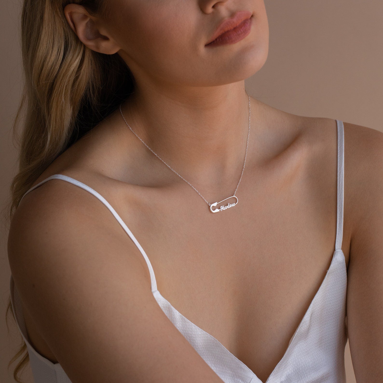 A woman in a white camisole wears a delicate silver Safety Pin Name Necklace featuring a personalized name pendant, making it a subtle statement accessory.