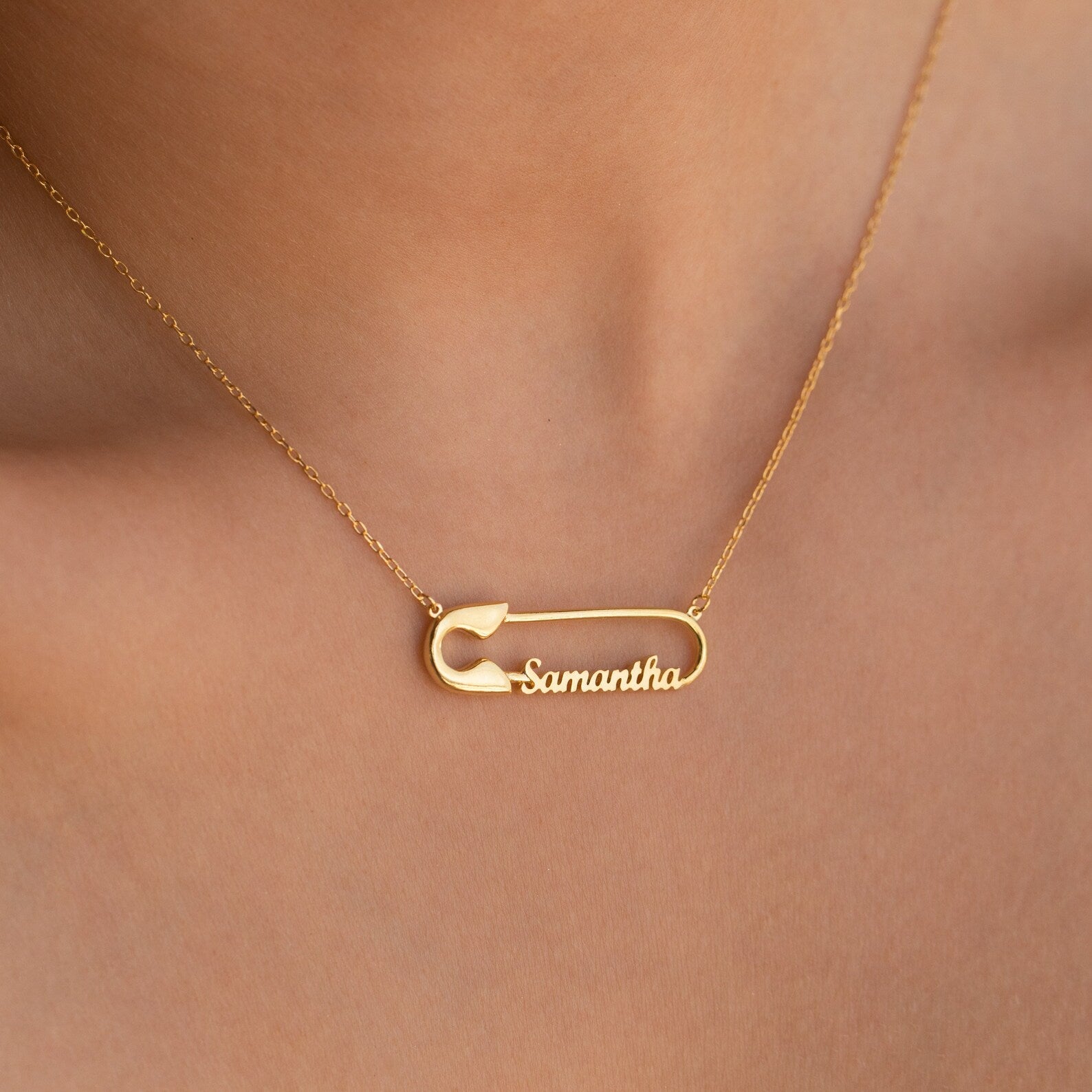 The Safety Pin Name Necklace, featuring "Samantha" and worn around the neck, is a unique personalized accessory that stands out as a statement piece.