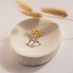 Gold and silver rings with crystal accents rest on a white ceramic dish beside dried grasses. The Starry Night Ear Cuffs, designed for a no-piercing look, complete this elegant display.