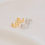 Two pairs of Claw Ear Cuffs, featuring minimalist designs in gold and silver, are displayed on a soft beige surface.