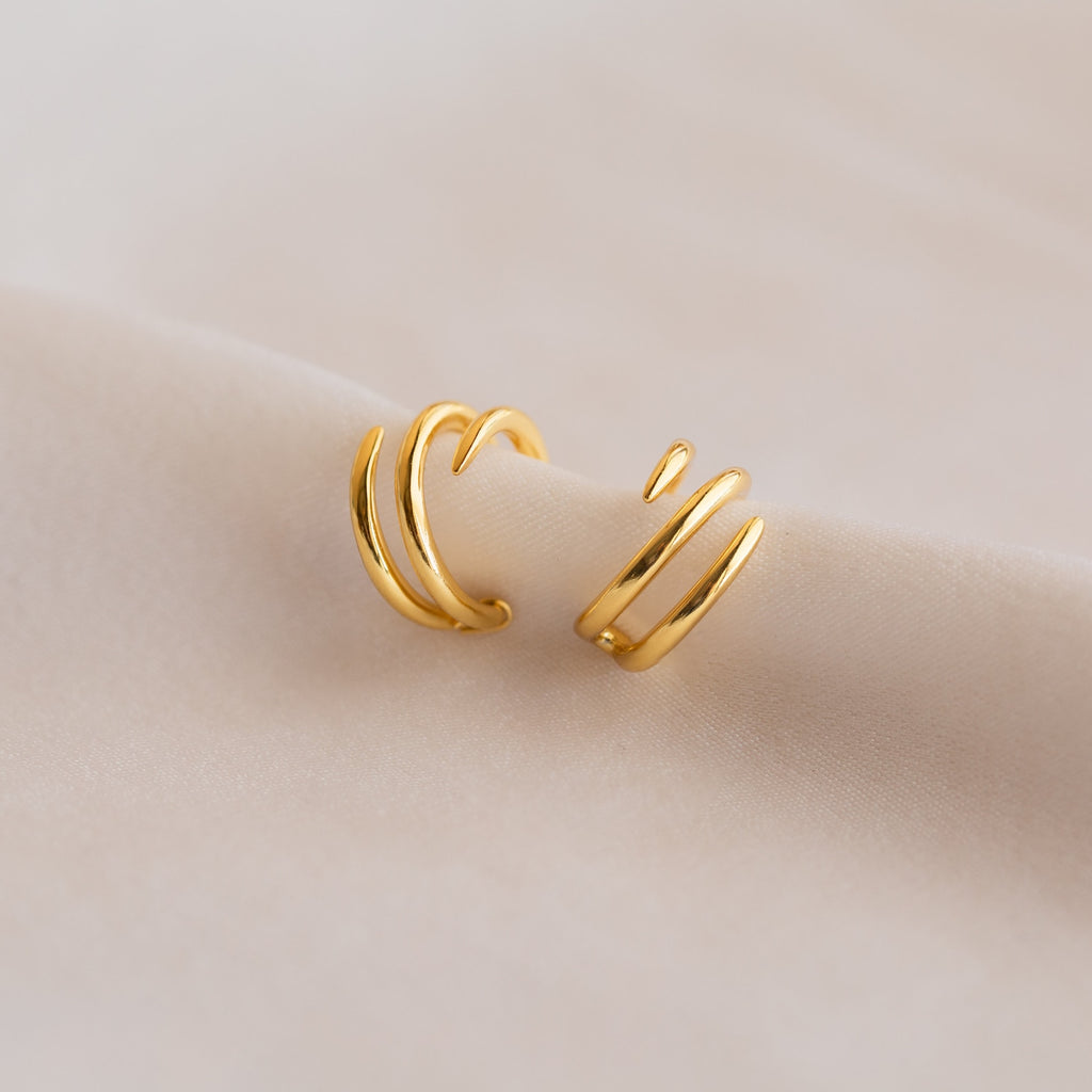Two Claw Ear Cuffs in gold with a spiral shape are displayed on a soft, light beige fabric, offering a subtle way to enhance your earring style.
