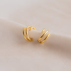 Two Claw Ear Cuffs in gold with a spiral shape are displayed on a soft, light beige fabric, offering a subtle way to enhance your earring style.