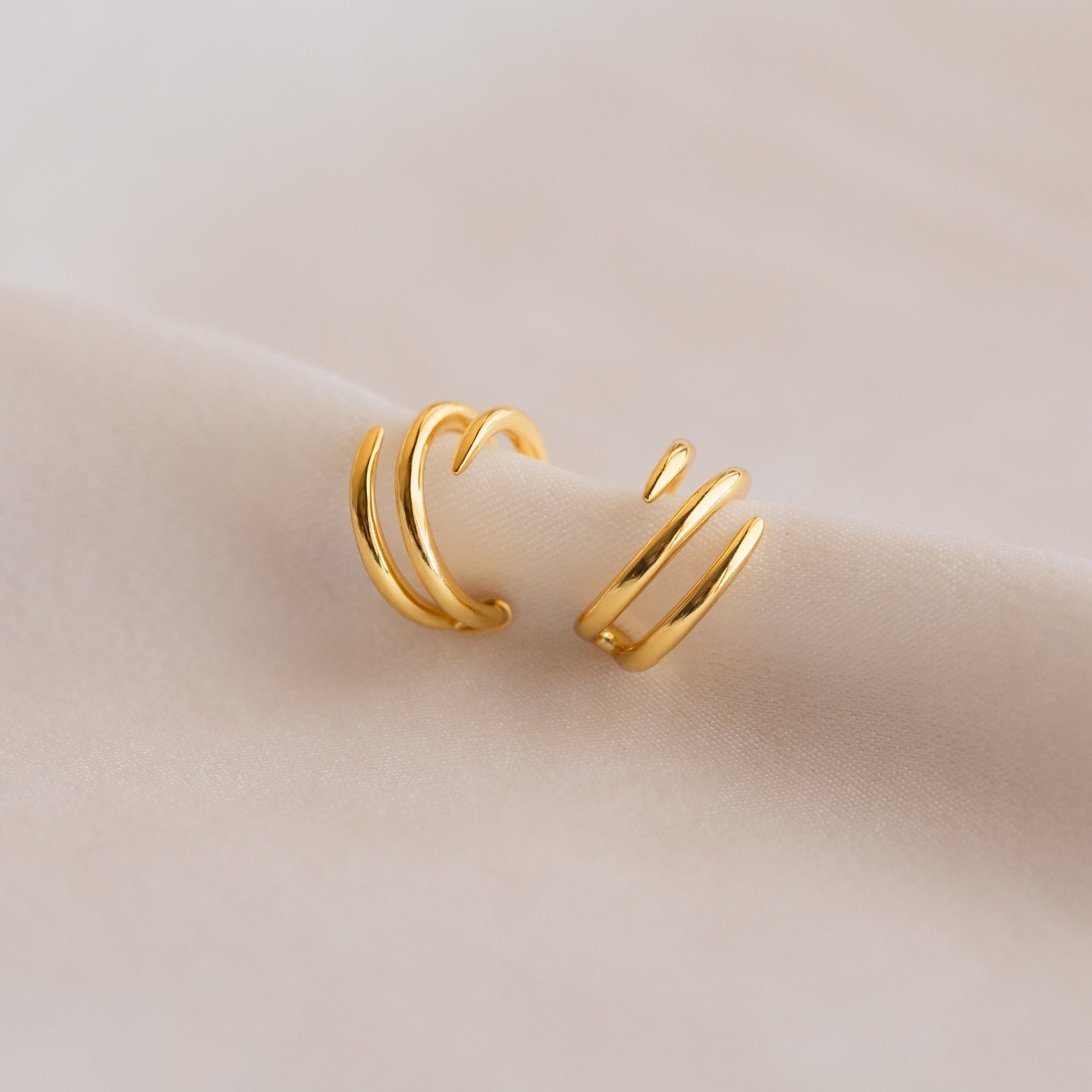 Two Claw Ear Cuffs in gold with a spiral shape are displayed on a soft, light beige fabric, offering a subtle way to enhance your earring style.