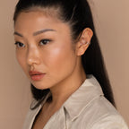 A woman with long dark hair wearing a beige top and a silver Claw Ear Cuff gazes to the side against a tan background.
