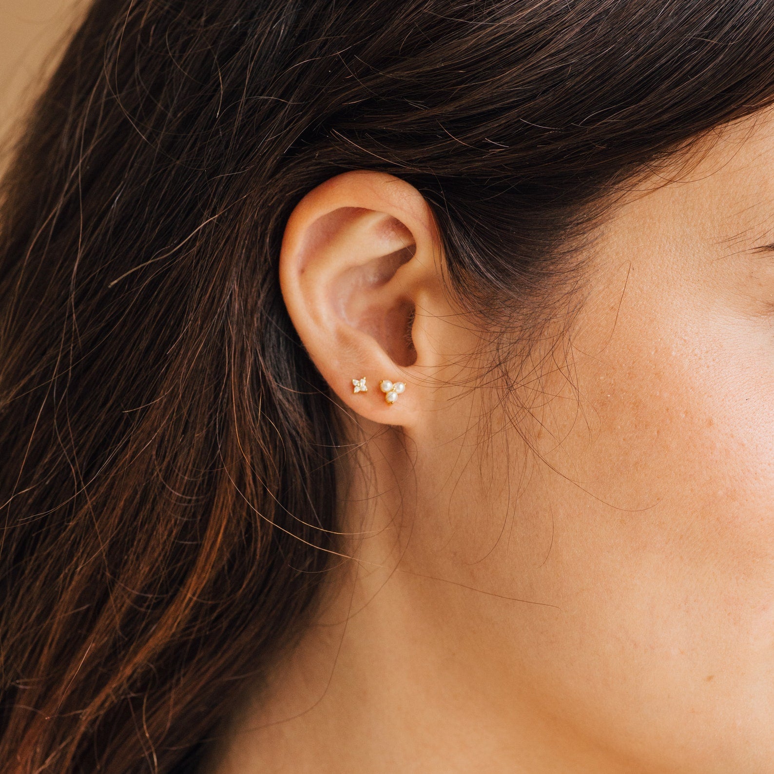 Close-up of a woman's ear wearing Maud Pearl Studs—elegant gold earrings featuring a star and three-circle design, perfect as a timeless luxury gift.