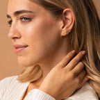 A blonde woman poses against a beige background, wearing Constellation Earrings and touching her hair.