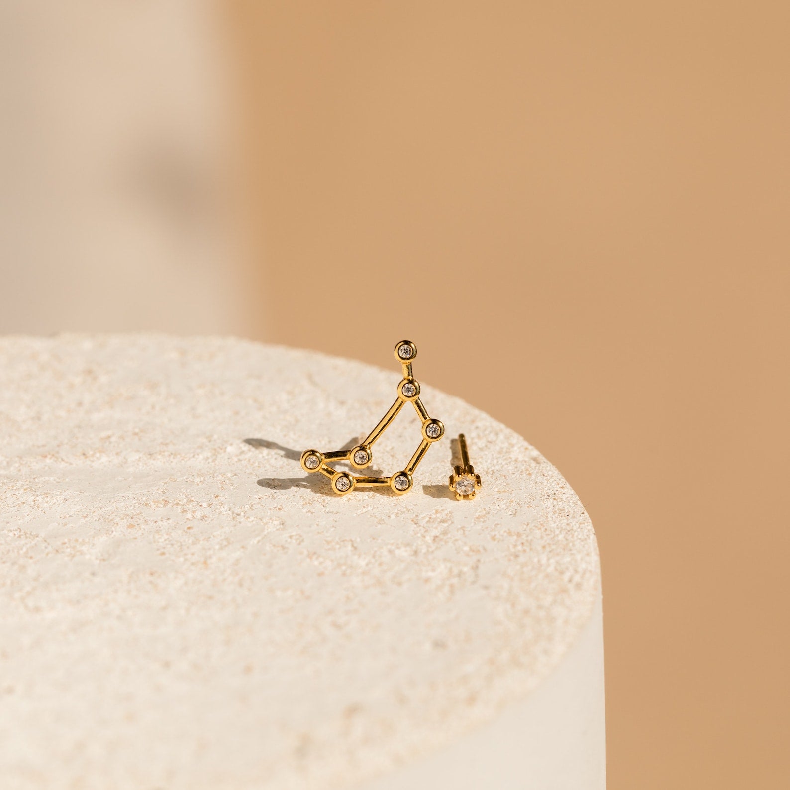 Constellation Earrings with small stones, displayed on a textured beige surface and minimalist background—ideal for fans of astrology-inspired style.