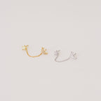 The Luna Moon & Star Chain Earrings feature two pairs—one gold, one silver—linked by delicate chains, ideal for adding celestial style to your cartilage piercing. Shown on a light background.