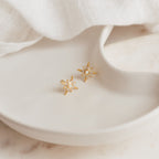 Starburst Studs featuring pearls and sparkling crystals, inspired by opal designs, shown on a white ceramic dish with a soft fabric background.