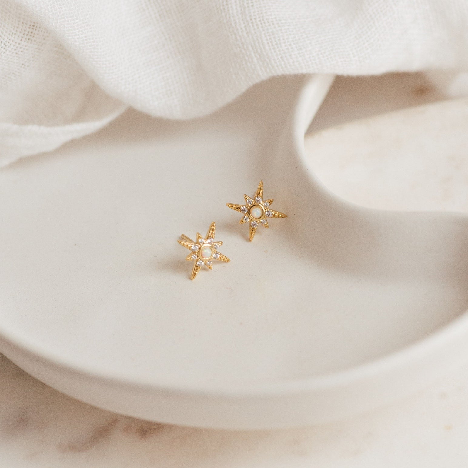 Starburst Studs featuring pearls and sparkling crystals, inspired by opal designs, shown on a white ceramic dish with a soft fabric background.