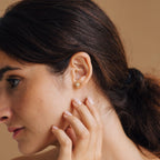 A woman with her hair tied back touches her ear, showcasing the gold Starburst Studs against a neutral background.