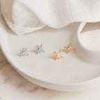 Two pairs of Starburst Studs, in silver and gold, are displayed on a white ceramic dish—perfect for adding celestial sparkle to your earring collection.