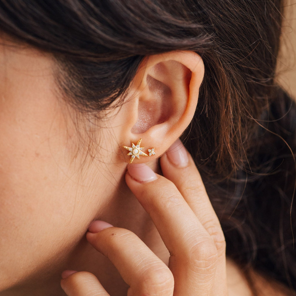 A close-up shows a woman’s ear adorned with Starburst Studs as her hand gently touches her earlobe.