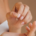 A hand with manicured nails holds a gold Striker Pave Huggie earring in soft lighting, showcasing these stylish, trendy earrings.