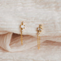 The Florence Diamond Chain Earrings, featuring delicate hanging chains and sparkling diamond accents, are displayed on a soft, cream-colored fabric.