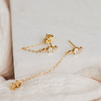 Florence Diamond Chain Earrings featuring gold studs, dangling chains, and crystal accents, displayed on marble with soft fabric.
