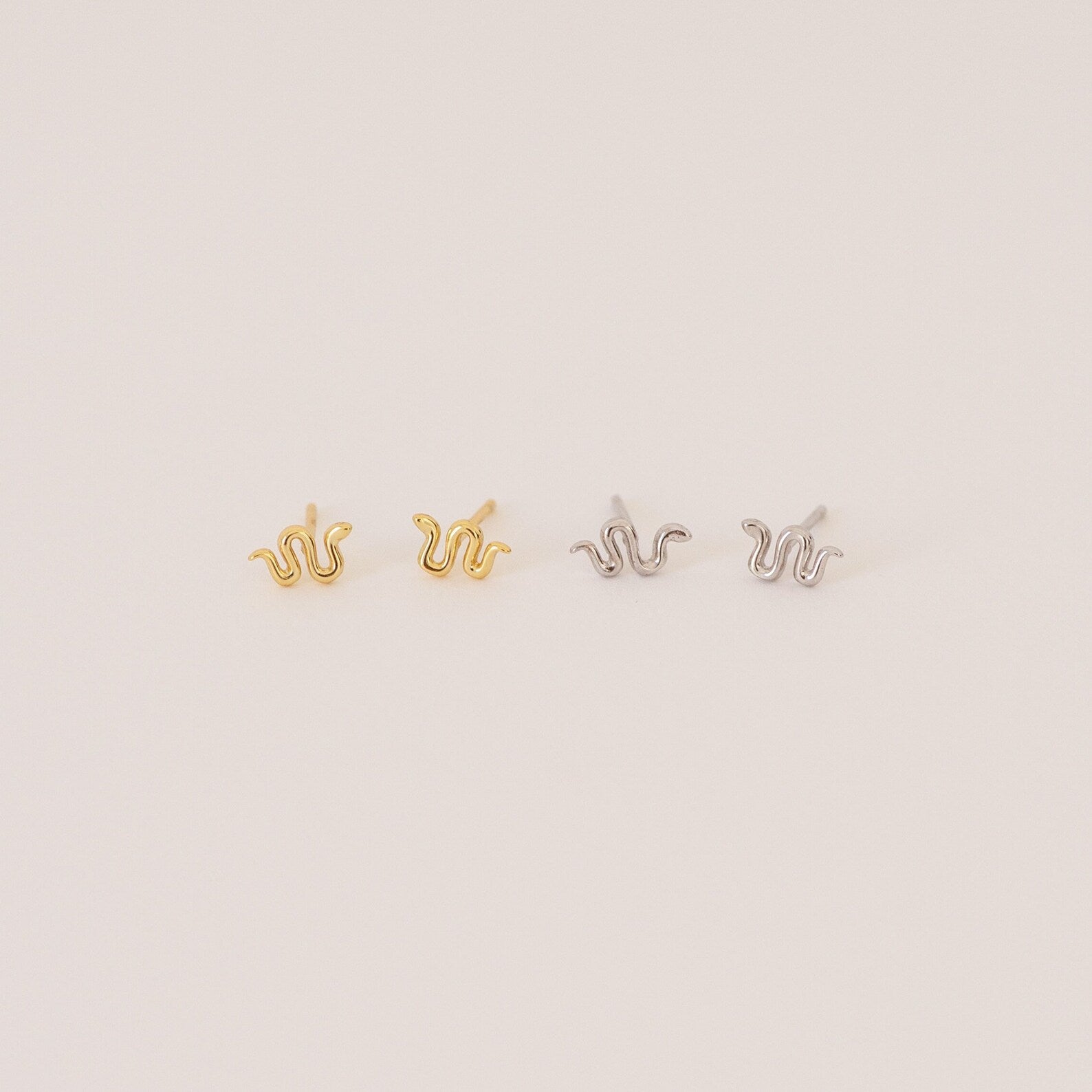 The Tiny Python Studs feature a chic snake design in gold and silver, adding subtle edge to your style. Perfect for boho-luxe earring lovers, these dainty studs are set against a light, neutral backdrop.