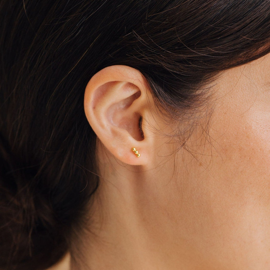 Close-up of a woman's ear wearing Trio Beaded Bar Studs in gold—minimalist earrings perfect for everyday style.