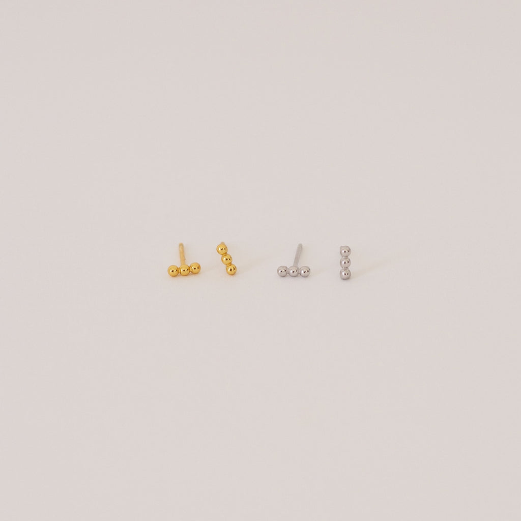 Two pairs of Trio Beaded Bar Studs—one gold, one silver—each featuring three round beads. These minimalist earrings are perfect for everyday wear and are shown against a plain background.