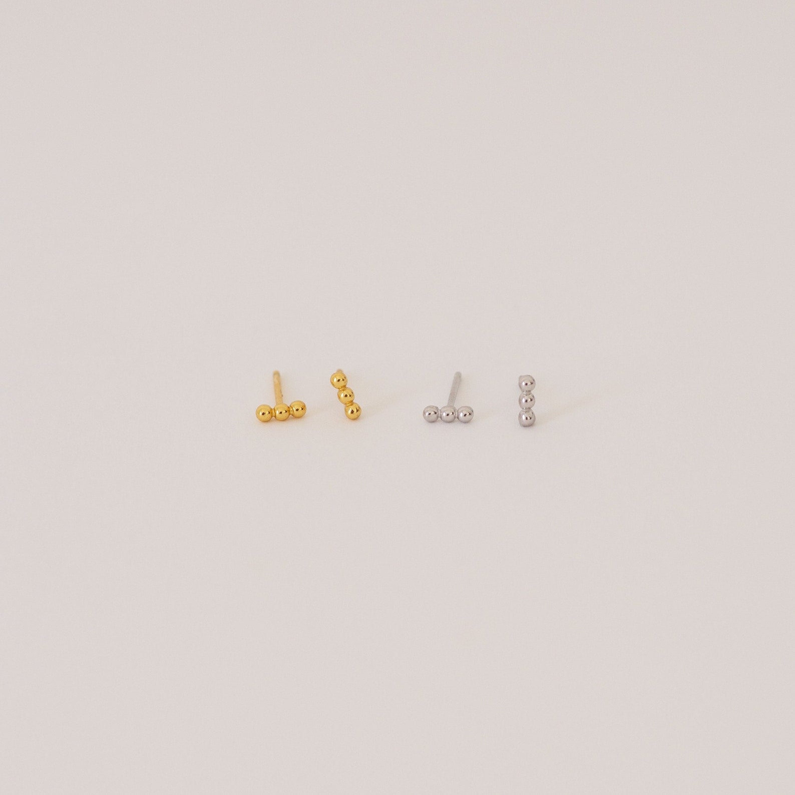 Two pairs of Trio Beaded Bar Studs—one gold, one silver—each featuring three round beads. These minimalist earrings are perfect for everyday wear and are shown against a plain background.