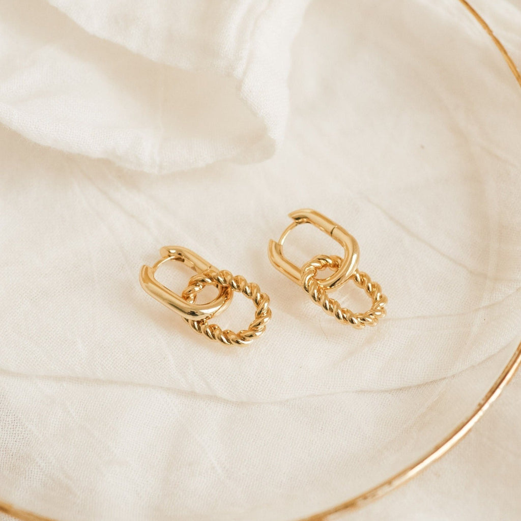 The Kenzie Chain Link Earrings rest on a white fabric surface with a delicate sheer cloth beside them—perfect statement earrings for those who love edgy jewelry.