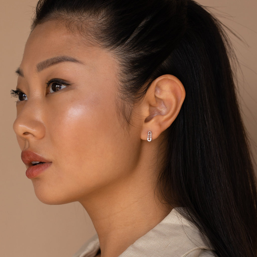Woman with long dark hair in a ponytail, wearing Tiny Pave Safety Pin Studs, looking to the left.