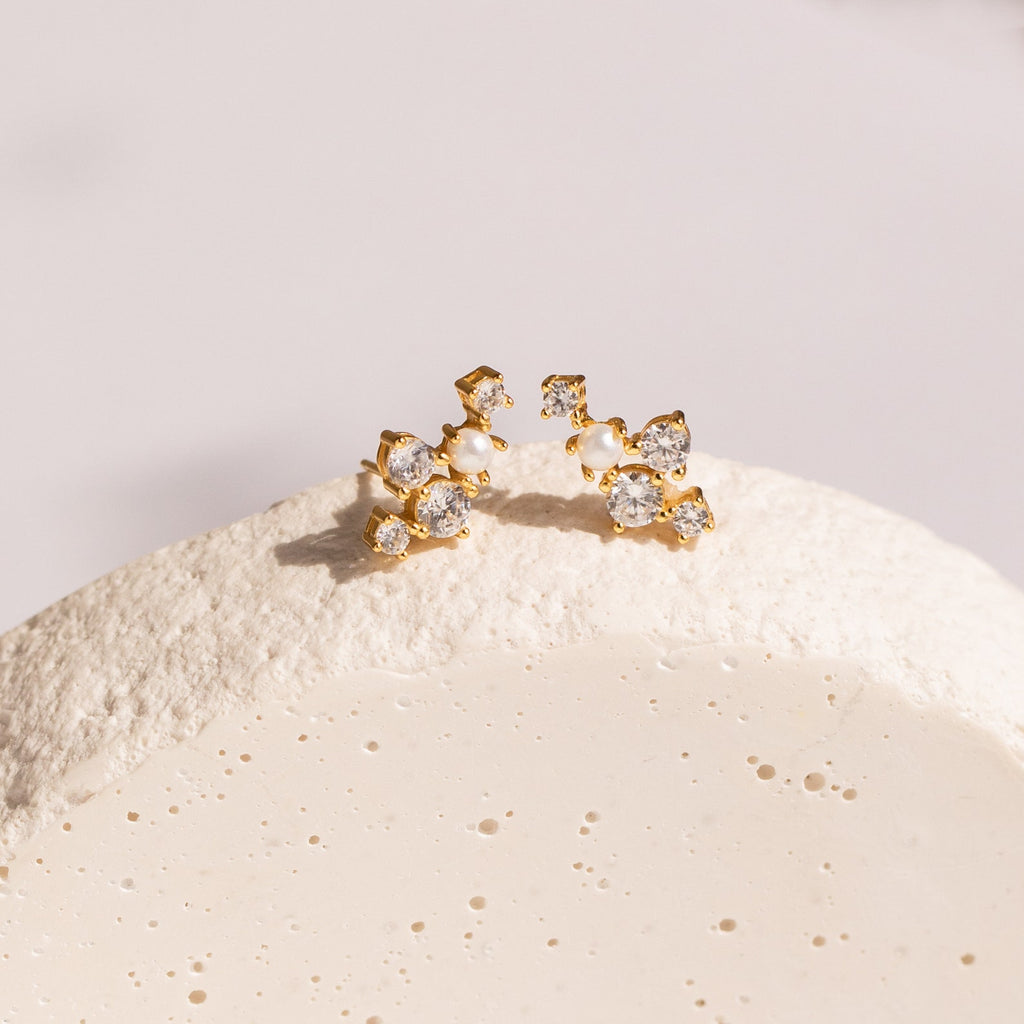 Seine Diamond Studs featuring clusters of clear gemstones and a cultured pearl, beautifully arranged on a textured white surface—ideal as elegant wedding earrings.