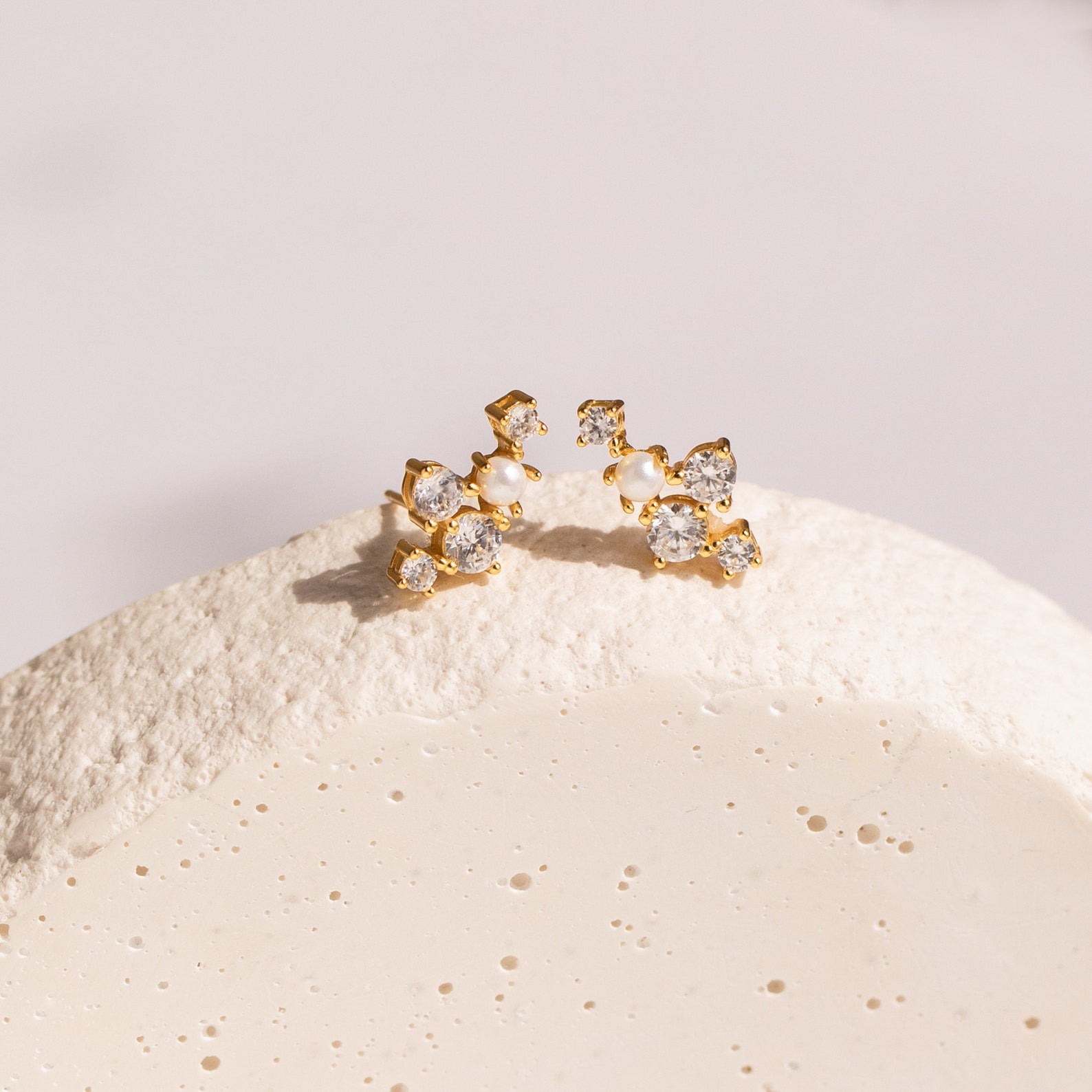 Seine Diamond Studs featuring clusters of clear gemstones and a cultured pearl, beautifully arranged on a textured white surface—ideal as elegant wedding earrings.