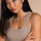 A woman in a beige knit tank top poses against a beige background, accessorized with the Emerald Station Necklace featuring delicate emerald green beads for a boho touch.