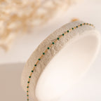 The Emerald Station Necklace features a delicate gold chain adorned with small emerald green beads, presented on a textured white stand.