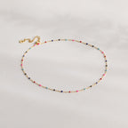 The Rainbow Station Necklace features a delicate gold chain with small, colorful beads evenly spaced along its length, shown on a light background.